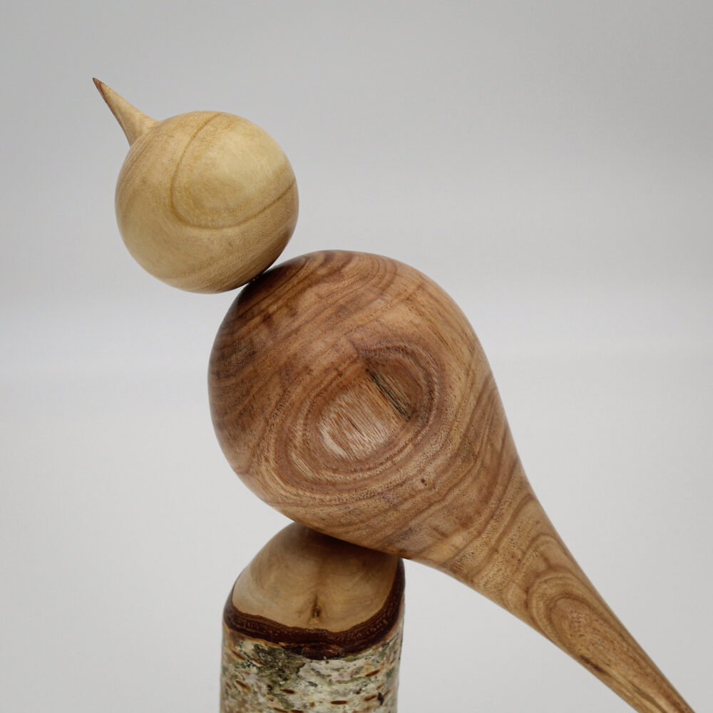 Oiseau décoratif en bois d'albizia et d'if sur son socle en bois de bouleau gros plan